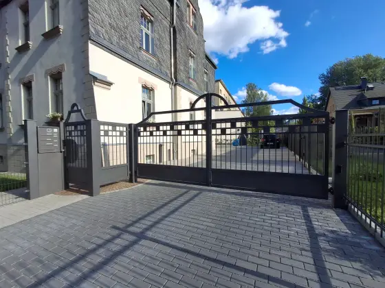 Stahltor mit geschwungenem Bogen und passender Zaunanlage vor einem Altbau